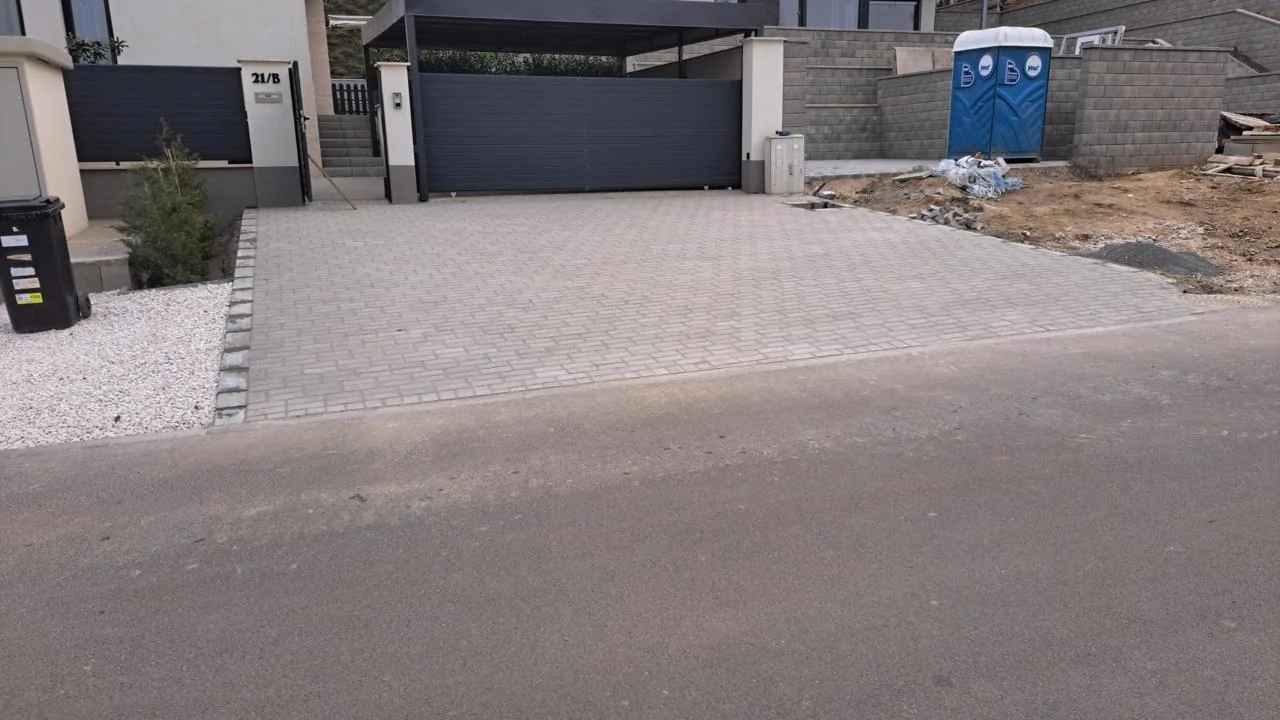 Világosszürke térköves kocsibeálló modern sötét kapu előtt