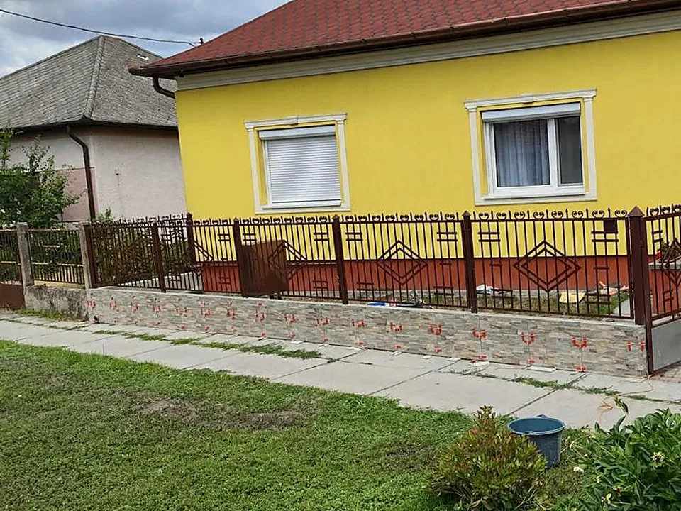 Sötétbarna fémkerítés terméskővel burkolt lábazaton